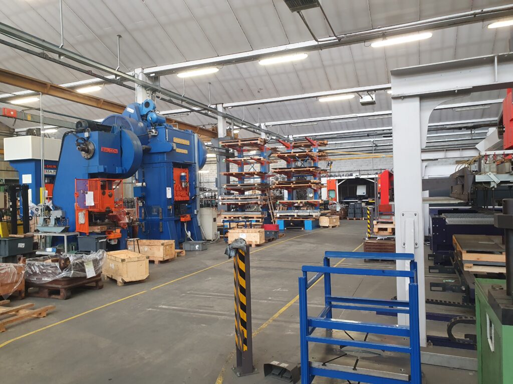 Interno di stabilimento industriale con macchinari pesanti e area di stoccaggio materiali.